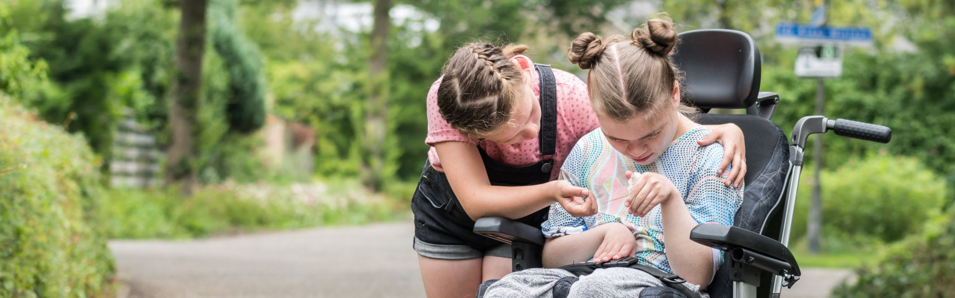 disabled child in a wheelchair being cared for by her younger sister