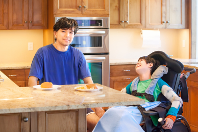 smiling young boy sitting in his wheelchair with his brother